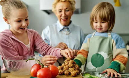 Två barn som gör vegobullar med äldre dam